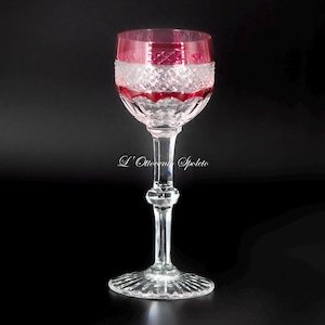 Può includere: Un calice da vino in cristallo trasparente con un bordo rosso intenso e una fascia di motivi a diamante intagliati. Lo stelo è sfaccettato con un nodo esagonale centrale e la base circolare presenta un disegno a raggiera. Testo L'Ottocento Spoleto.