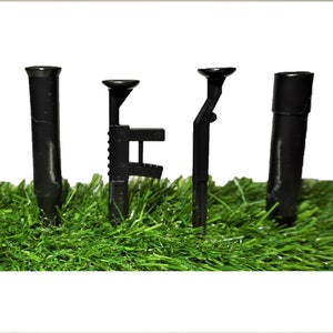 May include: Four black plastic toy guns, including a rifle, a pistol, and two pipes, are displayed on a bed of green artificial grass.