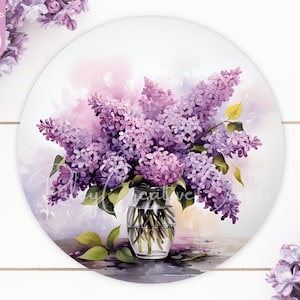 Könnte beinhalten: Ein Strauß lilafarbener Fliederblüten in einer klaren Glasvase auf weißem Holzgrund. Die Blumen sind in einem lockeren, natürlichen Stil angeordnet, und die Vase ist schlicht und elegant.
