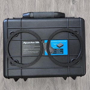 May include: A black rectangular Apache 3800 protective case with a top handle and two circular black foam rings placed on the front. The case features a blue informational label with white text detailing product specifications and features.