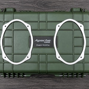 May include: An olive green rectangular hard-shell protective case with a grid-patterned exterior and two heavy-duty latches. The center features a black label with the white text Apache 4800 Rugged Mobility. Two white oval speaker mounting rings.