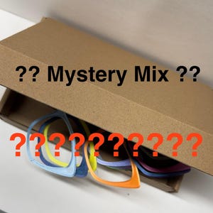 May include: A cardboard box with the text "?? Mystery Mix ??" and several pairs of colorful eyeglass frames. The frames are in various colors, including blue, yellow, and orange, with question marks in red.