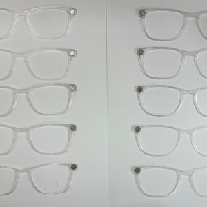 May include: Ten pairs of clear plastic eyeglasses with silver accents on a white background.