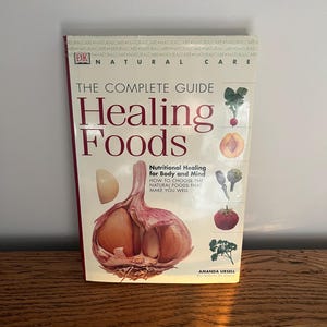May include: A red and white book titled "The Complete Guide Healing Foods" with a picture of a cut open garlic clove on the cover. The book subtitle is "Nutritional Healing for Body and Mind" and the text "How to choose the natural foods that make you well" is also on the cover. The author is Amanda Ursell.