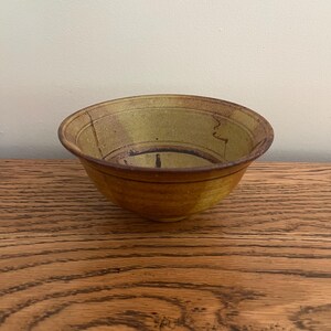 May include: A small, yellow ceramic bowl with brown and black glaze. The bowl has a rounded shape and a slightly flared rim.