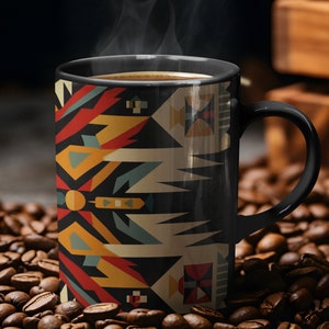 May include: A black coffee mug with a geometric pattern in shades of red, yellow, blue, and white. The mug is filled with coffee and steam is rising from the top. The mug is sitting on a bed of coffee beans.