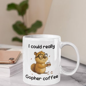 May include: White ceramic coffee mug with a cartoon gopher wearing glasses and holding a cup of coffee. The mug reads "I could really gopher coffee".