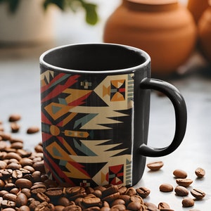 May include: A black coffee mug with a geometric pattern in shades of red, yellow, blue, and white. The mug is sitting on a pile of coffee beans.