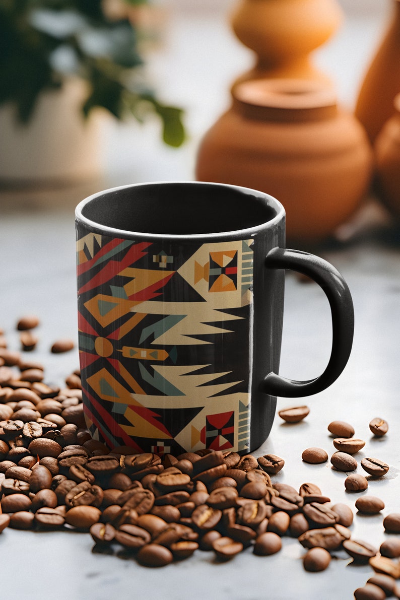 May include: A black coffee mug with a geometric pattern in shades of red, yellow, blue, and white. The mug is sitting on a pile of coffee beans.