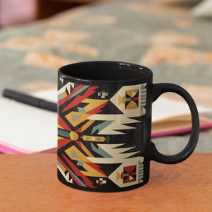 May include: Black ceramic mug with a geometric pattern in shades of red, yellow, blue, and white on a black background. The pattern is reminiscent of Native American art.