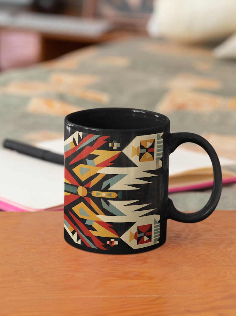 May include: Black ceramic mug with a geometric pattern in shades of red, yellow, blue, and white on a black background. The pattern is reminiscent of Native American art.