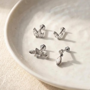 Puede incluir: Cuatro piezas de joyer&iacute;a plateada con piedras preciosas claras y brillantes. Dos piezas presentan un dise&ntilde;o en forma de hoja, una con forma de l&aacute;grima colgante, y la &uacute;ltima tiene un grupo de piedras. La joyer&iacute;a se exhibe en un plato blanco poco profundo.