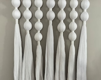 May include: White macrame wall hanging with multiple strands of yarn and white pom poms.