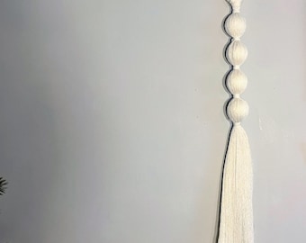 May include: White macrame wall hanging with a wooden ring at the top and four white yarn balls hanging from it.