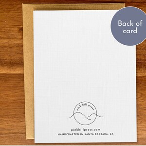 May include: The back of a white card with a brown envelope. The card features a black and white logo with the text "pink hill press" and the website address "pinkhillpress.com". The text "HANDCRAFTED IN SANTA BARBARA, CA" is also printed on the card.