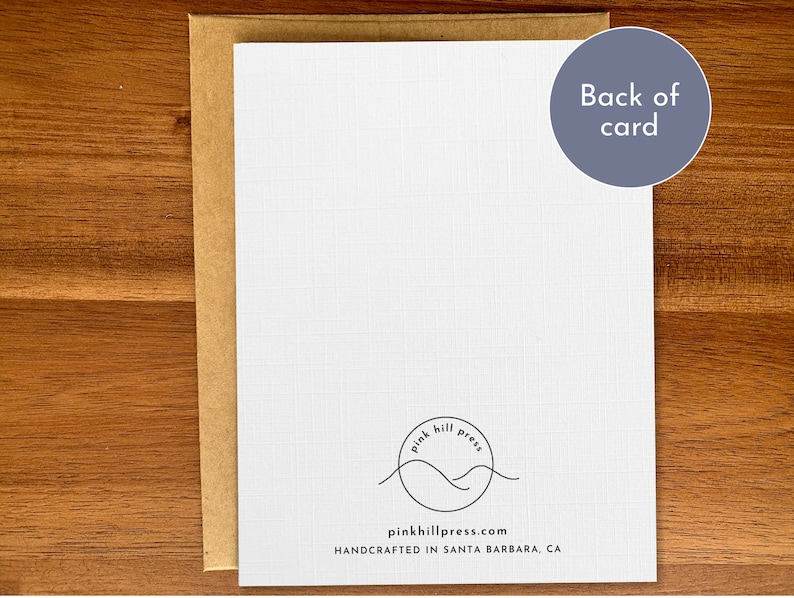 May include: The back of a white card with a brown envelope. The card features a black and white logo with the text "pink hill press" and the website address "pinkhillpress.com". The text "HANDCRAFTED IN SANTA BARBARA, CA" is also printed on the card.