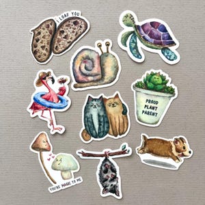 Op de afbeelding: Set van 10 kleurrijke geïllustreerde stickers met verschillende ontwerpen, waaronder een slak, een schildpad, een flamingo, een paddenstoel, een potplant, twee katten, een opossum en een brood. De stickers hebben verschillende teksten, waaronder "I loaf you", "Proud Plant Parent" en "You're magic to me".