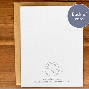 May include: The back of a white card with a brown envelope. The card has a black and white logo with the text "pink hill press" and the website address "pinkhillpress.com". The text "HANDCRAFTED IN SANTA BARBARA, CA" is printed below the logo.