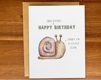 Może przedstawiać: Biała kartka z akwarelową ilustracją ślimaka. Tekst brzmi "(Belated) Happy Birthday" i "Sorry I'm a little slow."