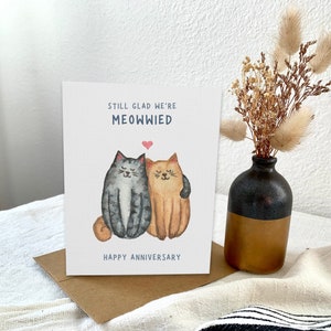 May include: A card with a watercolour illustration of two cats hugging. The text on the card reads "Still glad we're meowwied. Happy Anniversary."
