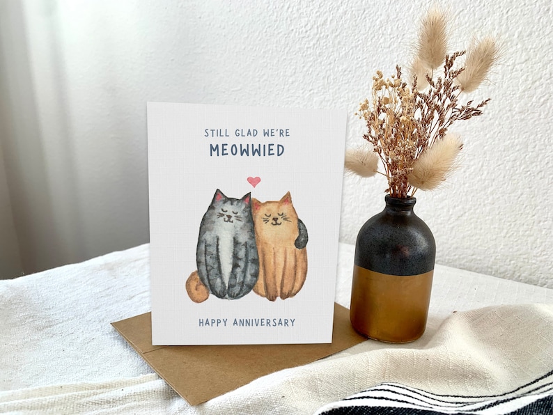 May include: A card with a watercolour illustration of two cats hugging. The text on the card reads "Still glad we're meowwied. Happy Anniversary."