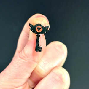 May include: Black metal key pin with a heart in the center of the keyhole. The heart is orange.