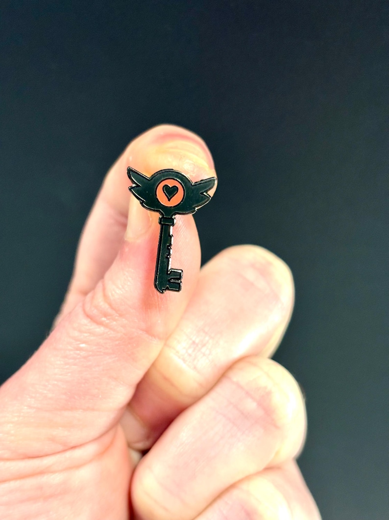 May include: Black metal key pin with a heart in the center of the keyhole. The heart is orange.