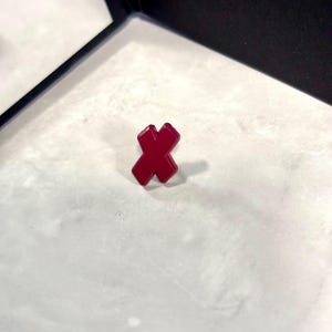 May include: A red, plastic, X-shaped pin.