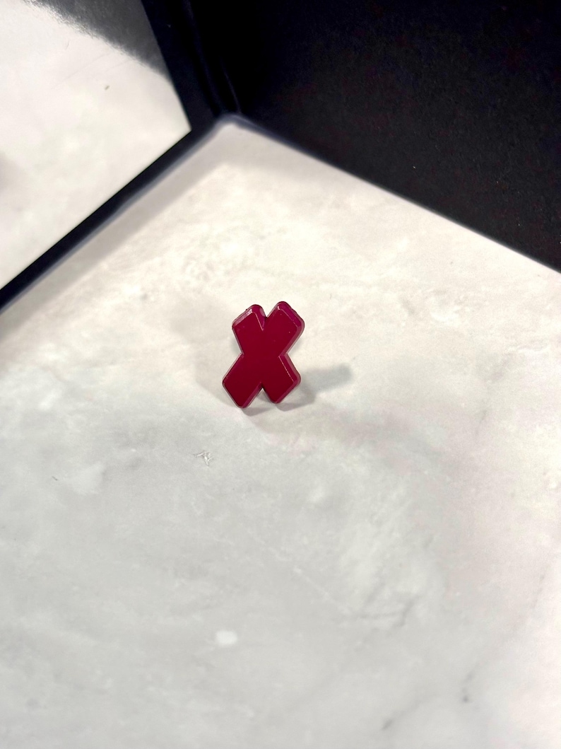 May include: A red, plastic, X-shaped pin.