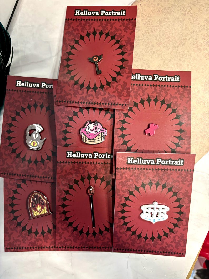 May include: Set of 7 Helluva Boss enamel pins featuring characters and objects from the show. The pins are on red cards with a black floral pattern and the text "Helluva Portrait".