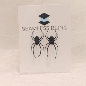 May include: A pair of black spider earrings on a white card with the text "Seamless Bling".