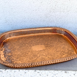 May include: A copper serving tray with a decorative, embossed design. The tray has a slightly oval shape and a raised rim.