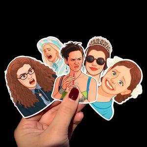 Puede incluir: Un conjunto de cinco pegatinas troqueladas con ilustraciones estilizadas de mujeres con diversas expresiones faciales. Las pegatinas representan a mujeres con expresiones de sorpresa, disgusto y alegría. Las pegatinas se sostienen sobre un fondo negro.