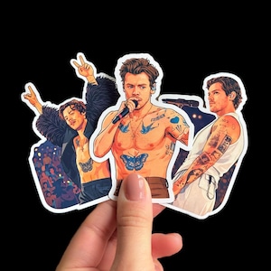 Puede incluir: Un conjunto de tres pegatinas con ilustraciones de un cantante. El cantante se muestra sin camisa con tatuajes, incluyendo una mariposa y la palabra "Fine Line". Una pegatina muestra al cantante con un micrófono.