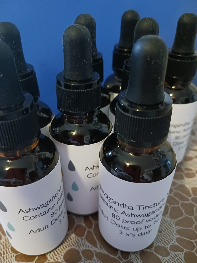 May include: A close-up of five amber glass bottles with dropper tops. The bottles are labeled with white labels that say "Ashwagandha Tincture" and "Contains: Ashwagandha 80 Proof Vodka Adult Dose: up to 10 drops 3 x's daily".