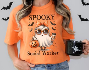 May include: A burnt orange t-shirt with a graphic of a ghost wearing sunglasses and a bow, holding a pumpkin and a coffee cup. The text "Spooky Social Worker" is printed on the shirt.