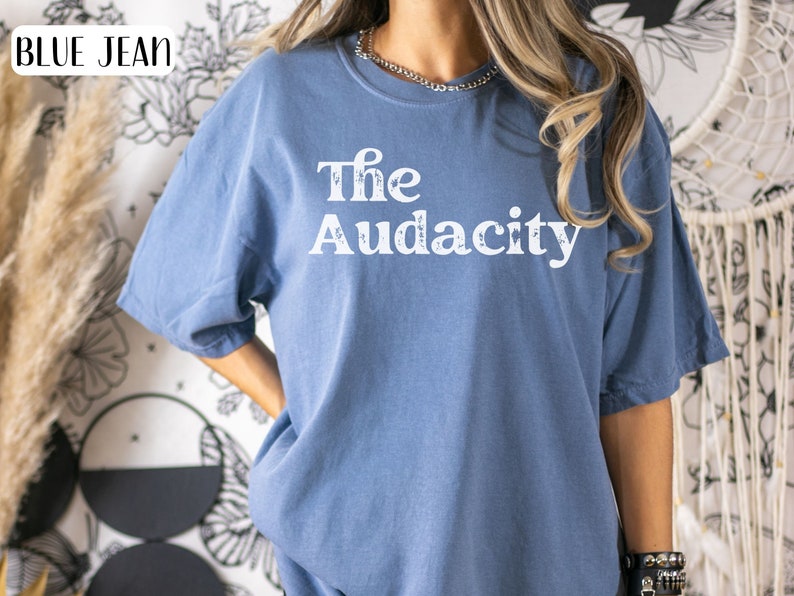 Puede incluir: Una camiseta de mezclilla azul con el texto "The Audacity" impreso en blanco en la parte delantera.