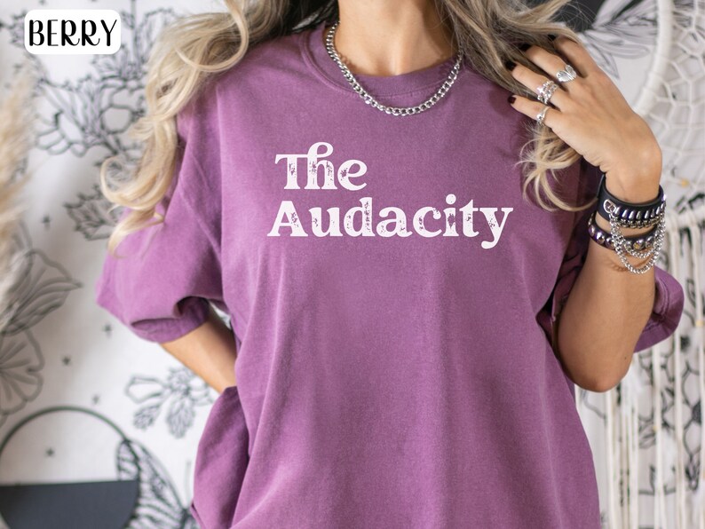 Puede incluir: Una camiseta morada con el texto "The Audacity" impreso en blanco en la parte delantera.