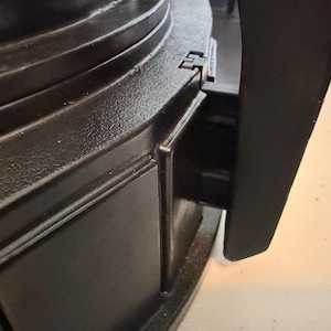 May include: A black plastic appliance component featuring a smooth, curved exterior surface with a vertical handle attachment. The structure displays a matte finish with molded rectangular panels and a visible hinge mechanism connecting the handle.