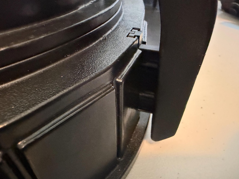 May include: A black plastic appliance component featuring a smooth, curved exterior surface with a vertical handle attachment. The structure displays a matte finish with molded rectangular panels and a visible hinge mechanism connecting the handle.