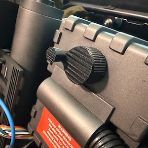 Puede incluir: Primer plano de un accesorio gris y negro con una perilla texturizada y una etiqueta de advertencia. El accesorio tiene forma rectangular con una serie de recortes cuadrados. La etiqueta de advertencia dice "WARNING FOR-043 ANGLE GEARBOX..."