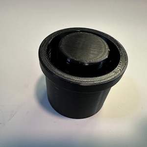 Op de afbeelding: Een zwarte plastic container met een deksel. De container heeft een getextureerde rand en het deksel heeft een glad oppervlak.