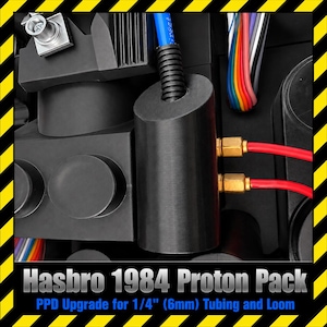 May include: A black cylindrical PPD upgrade component for a Hasbro 1984 Proton Pack, featuring a blue tube with black corrugated loom, two red tubes with brass fittings, and multi-colored wiring. The text reads: Hasbro 1984 Proton Pack PPD Upgrade for 1/4" (6mm) Tubing and Loom.