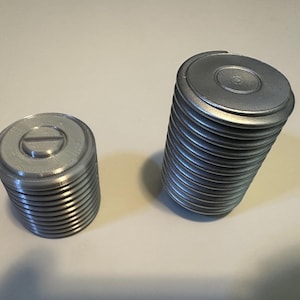 May include: Two silver metal containers with lids. The container on the right is taller and has a stack of lids. The container on the left is shorter and has a single lid.