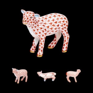 May include: A porcelain lamb figurine with a white base and a red and white patterned design. The lamb has gold accents on its hooves and ears. Three smaller lamb figurines are also visible.