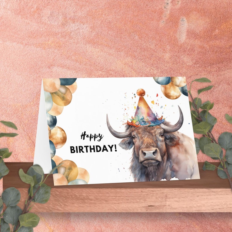 May include: A watercolor birthday card featuring a brown bull wearing a colorful party hat. The bull is surrounded by confetti and balloons in shades of gold, blue, and brown. The card reads "Happy Birthday!"