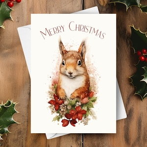 May include: A Christmas card featuring a watercolor illustration of a red squirrel with a white chest, surrounded by red berries and green leaves. The card has the text "Merry Christmas" in red lettering.