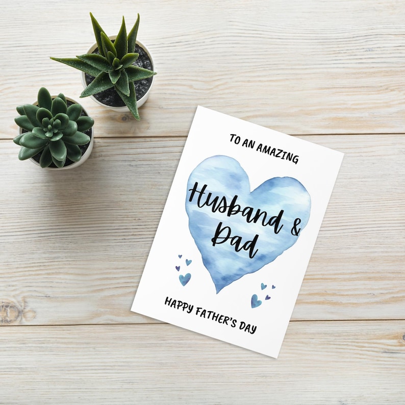 Puede incluir: Una tarjeta blanca con un coraz&oacute;n azul de acuarela que dice "Husband & Dad" y "To an amazing Husband & Dad Happy Father's Day".
