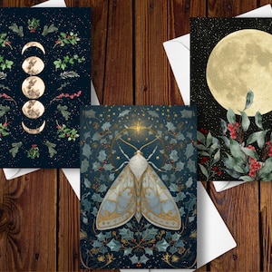 May include: Three art prints on white envelopes. One features moon phases and botanical elements on a dark blue background. Another showcases a moth with gold accents and botanical details. The third print displays a full moon with greenery and berries.
