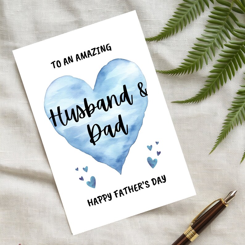 Puede incluir: Una tarjeta blanca con un coraz&oacute;n azul de acuarela que dice "To an amazing Husband & Dad" y "Happy Father's Day".